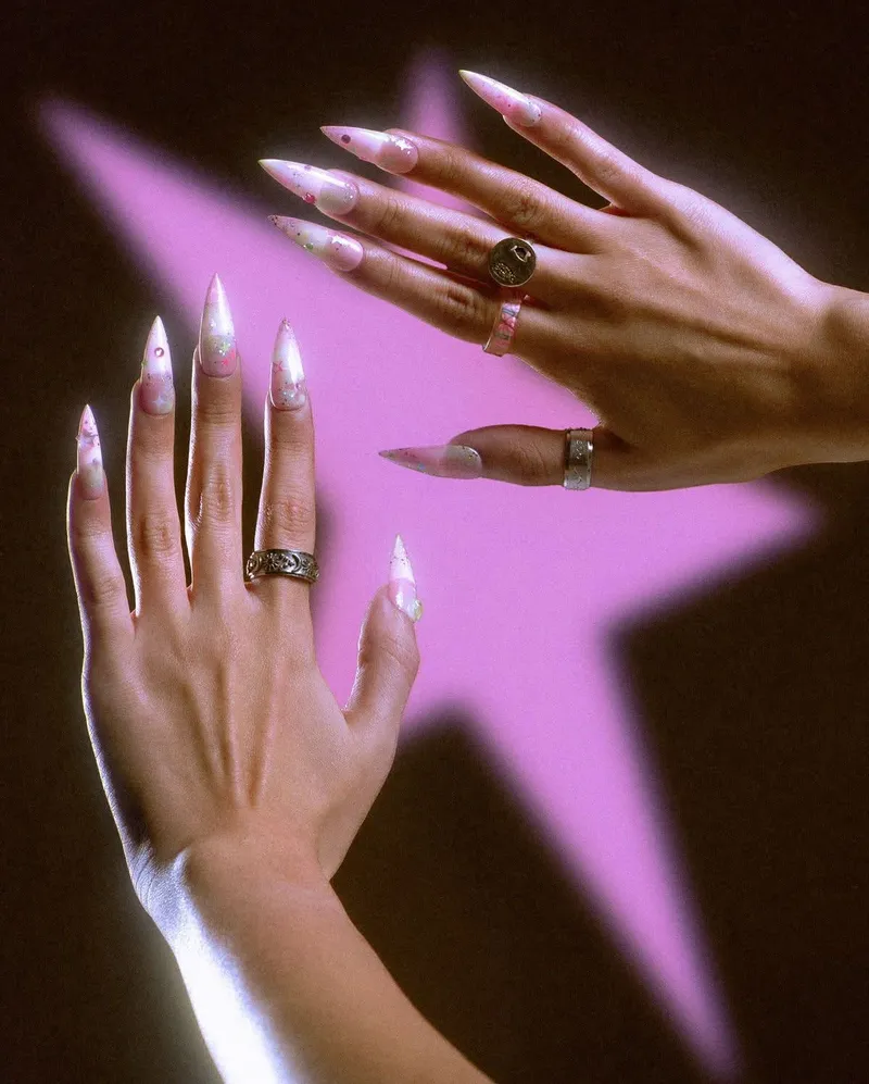 Ongles stiletto rose nacré à paillettes devant une étoile rose